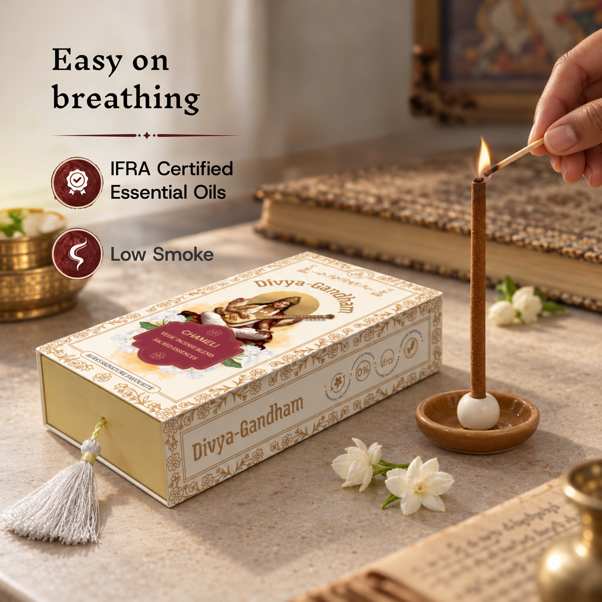 Hand lighting a Divyagandham Chameli incense stick highlighting easy breathing, IFRA certified essential oils, and low smoke, resting on a book beside the product box.