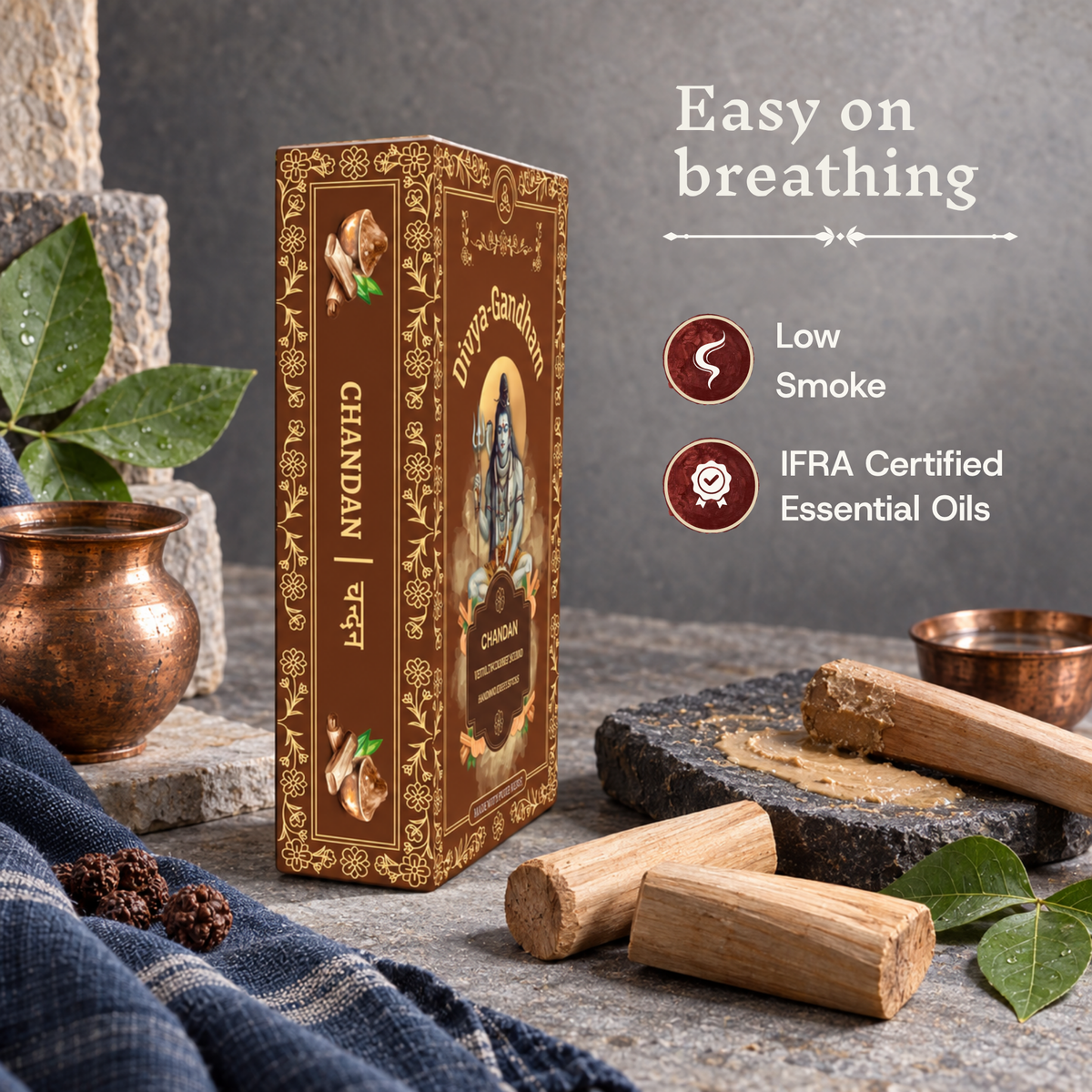 Divyagandham Chandan incense box highlighting easy breathing, IFRA certified essential oils, and low smoke, resting near sandalwood logs and a traditional stone grinder.