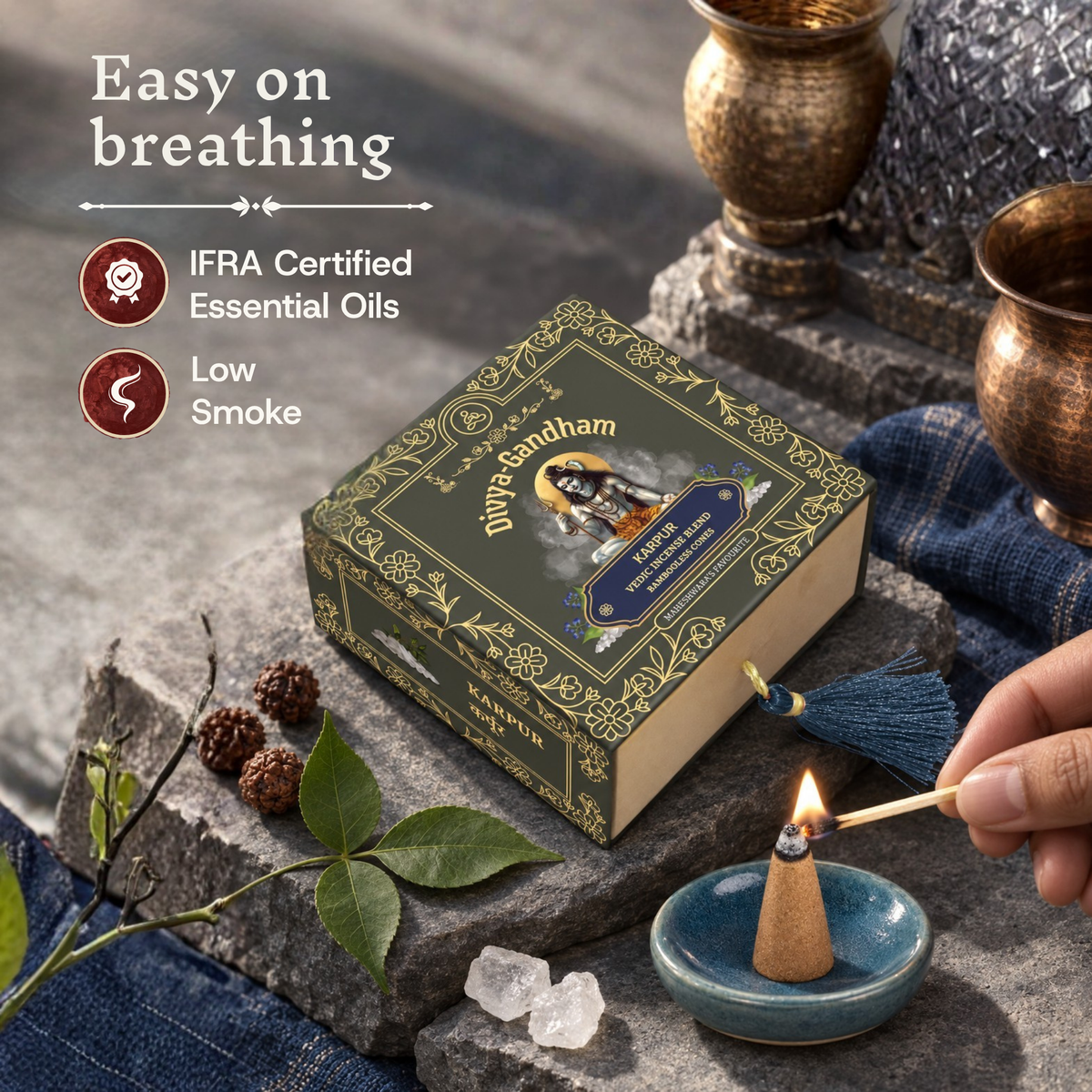 Hand lighting a Divyagandham Karpur incense cone highlighting easy breathing, IFRA certified essential oils, and low smoke, resting next to the product box on a stone surface.