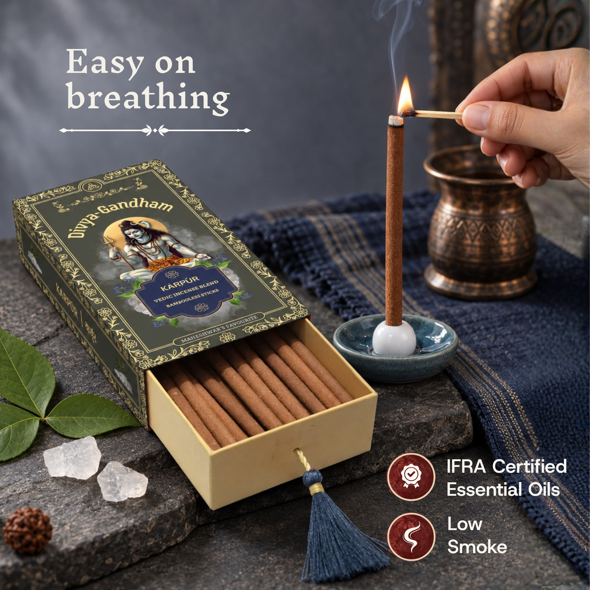 Hand lighting a Divyagandham Karpur incense stick highlighting easy breathing, IFRA certified essential oils, and low smoke, resting next to the open product box and camphor crystals.