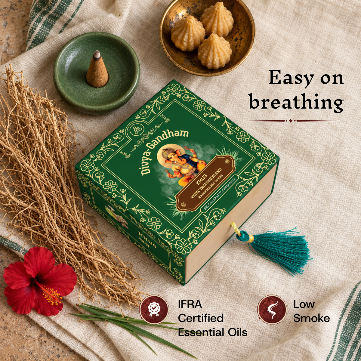 Lit Divyagandham Khus incense cone emphasizing easy breathing with low smoke and IFRA certified essential oils, arranged next to the green packaging, modaks, and vetiver.