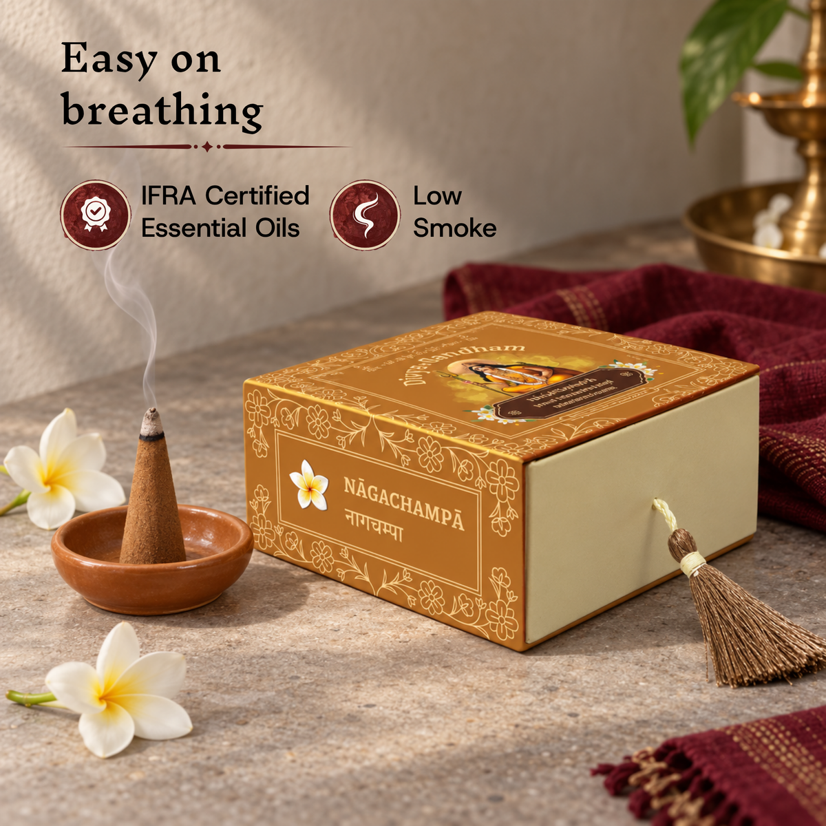 Lit Divyagandham Nagachampa incense cone highlighting easy breathing, IFRA certified essential oils, and low smoke, resting beside the product box.
