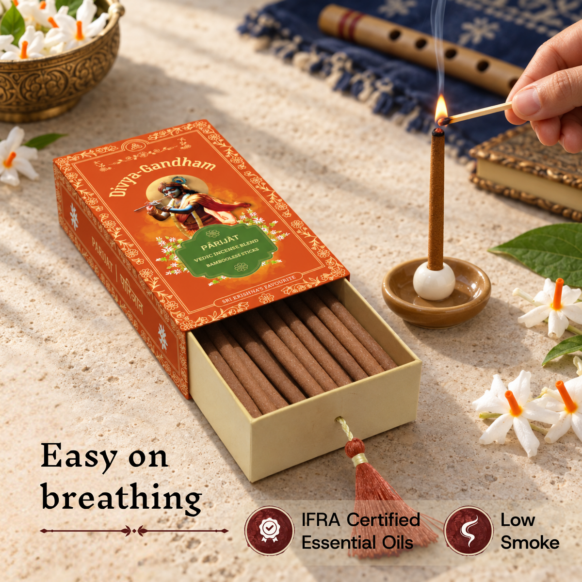 Hand lighting a Divyagandham Parijat incense stick highlighting easy breathing, IFRA certified essential oils, and low smoke, resting next to the product box and a book.