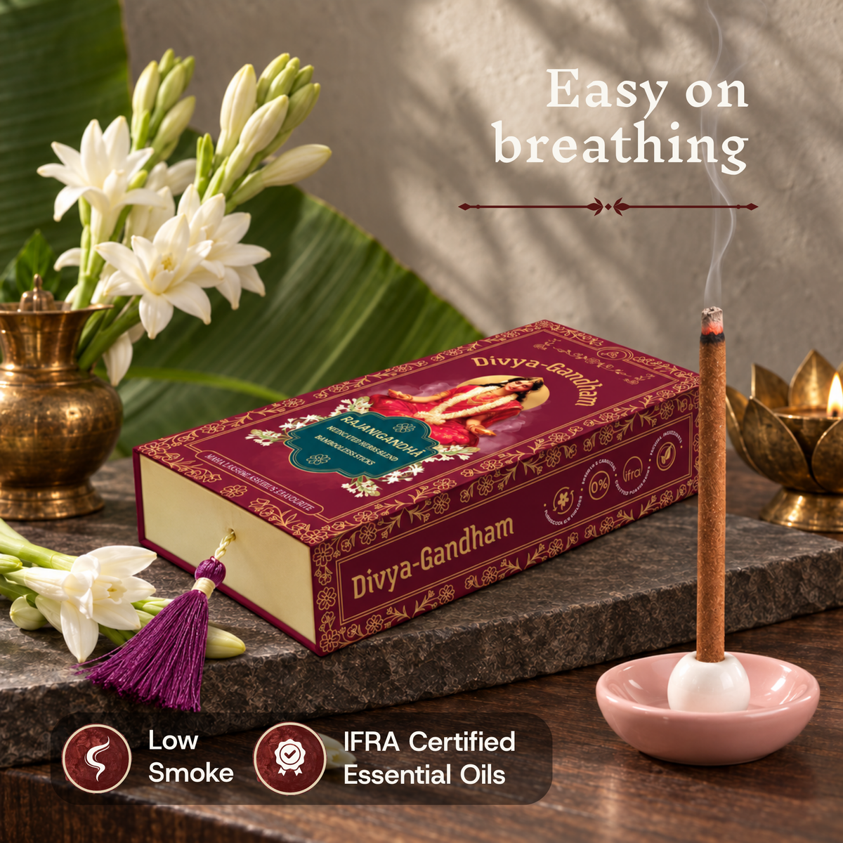 Hand lighting a Divyagandham Rajanigandha incense stick highlighting easy breathing, IFRA certified essential oils, and low smoke, resting on a stone surface near the open product box and fresh tuberose.
